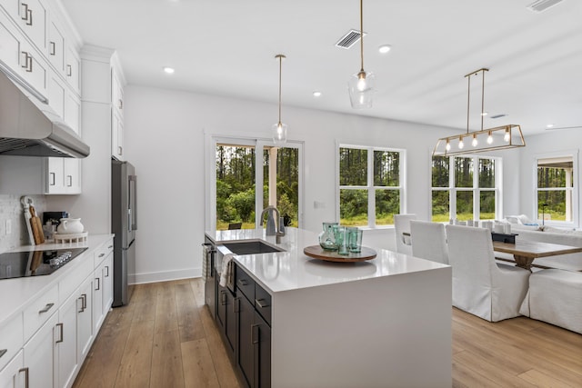 kitchen with black electric cooktop, open floor plan, a sink, freestanding refrigerator, and light countertops