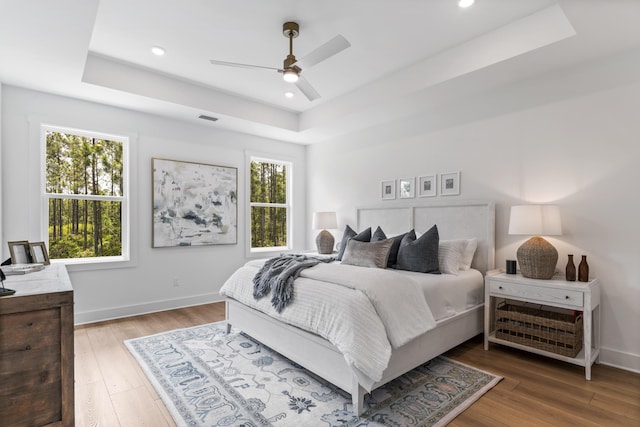 bedroom featuring a tray ceiling, multiple windows, light wood-style flooring, baseboards, and recessed lighting