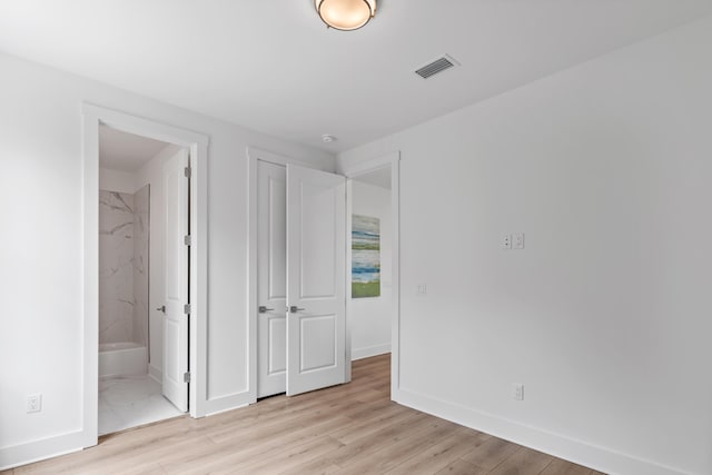 unfurnished bedroom featuring baseboards, light wood finished floors, and ensuite bath