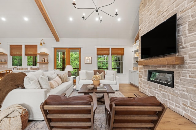 living area featuring light wood finished floors, a stone fireplace, a chandelier, beamed ceiling, and high vaulted ceiling