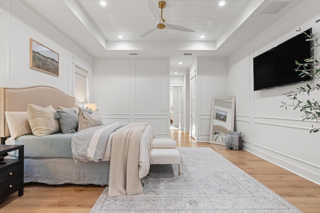bedroom featuring a decorative wall, a tray ceiling, light wood finished floors, recessed lighting, and wood ceiling