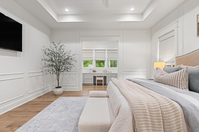 bedroom featuring a decorative wall, a tray ceiling, and light wood-style floors