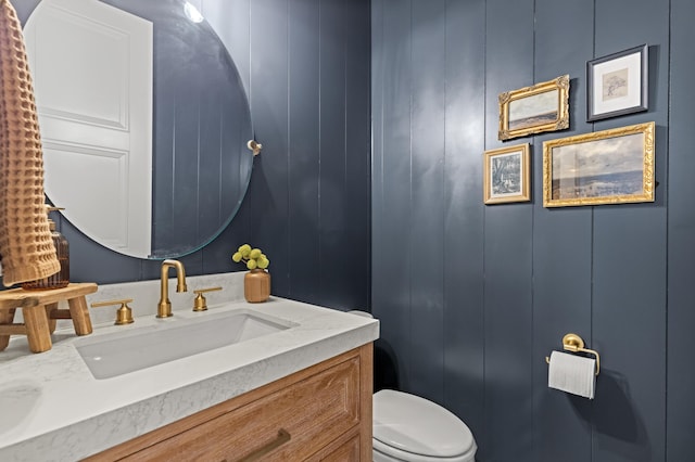 half bathroom featuring a decorative wall, toilet, and vanity