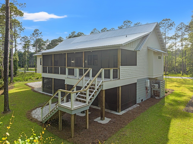 back of house featuring a sunroom, stairway, a lawn, and metal roof