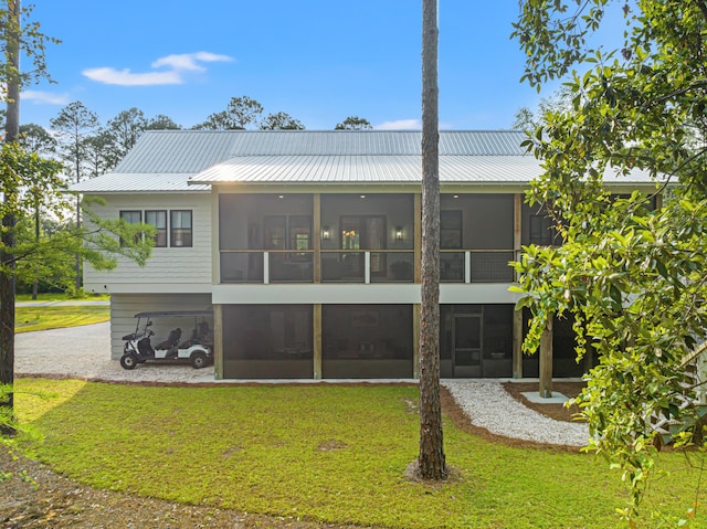 rear view of house with a sunroom, a yard, metal roof, and gravel driveway