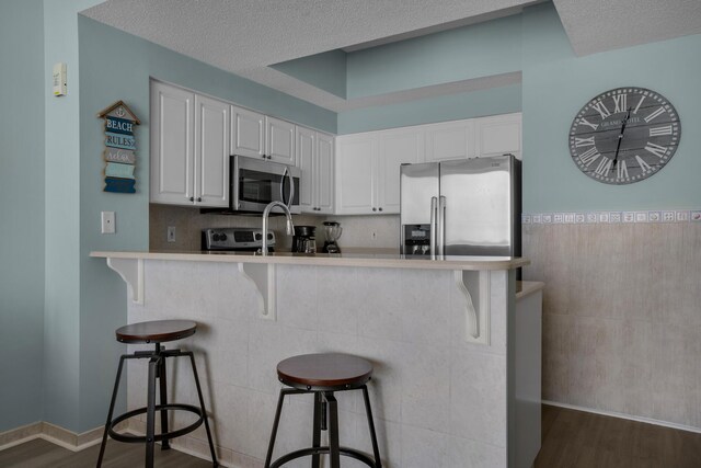 1200 Scenic Gulf Dr Unit B507, Miramar Beach, FL 32550 - kitchen featuring appliances with stainless steel finishes, dark wood-style flooring, a kitchen bar, and a textured ceiling