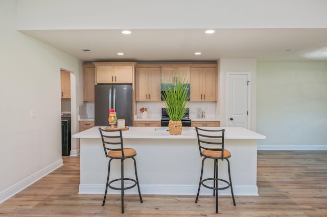 kitchen with freestanding refrigerator, black stove, a kitchen bar, light countertops, and recessed lighting