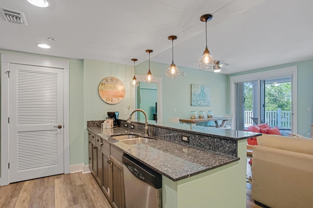 kitchen with stainless steel dishwasher, a sink, a peninsula, dark stone counters, and open floor plan