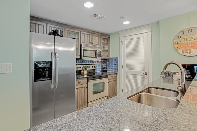 kitchen with stainless steel appliances, a sink, light stone countertops, glass insert cabinets, and recessed lighting