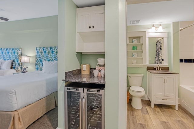 bedroom featuring wine cooler, light wood finished floors, ensuite bath, and a bar