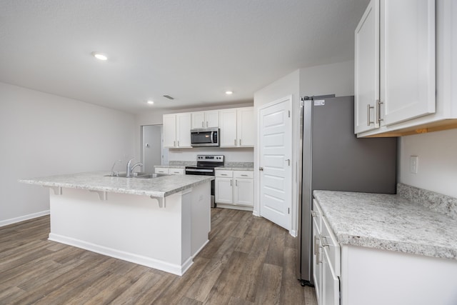 kitchen with appliances with stainless steel finishes, a sink, dark wood finished floors, white cabinets, and a kitchen breakfast bar