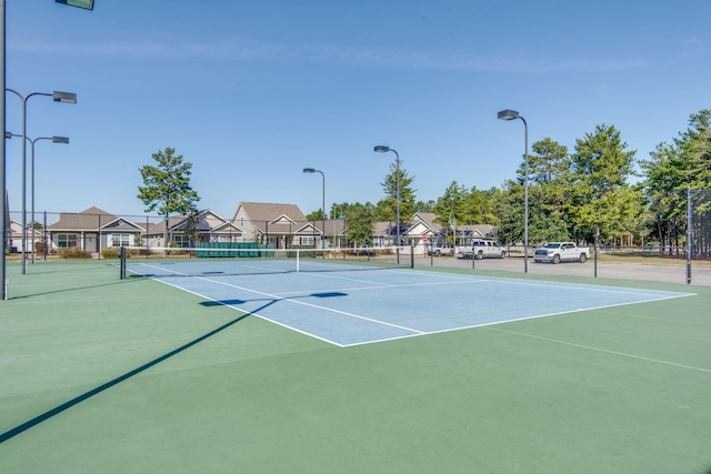 view of tennis court featuring community basketball court, fence, and a residential view