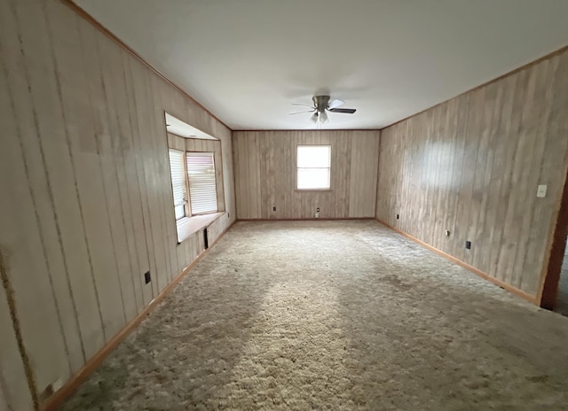 empty room with a ceiling fan, carpet flooring, and wood walls