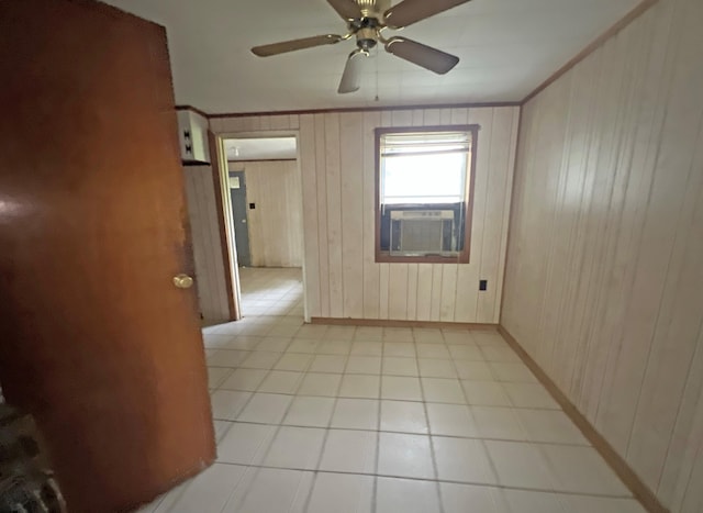 spare room with a ceiling fan, wood walls, baseboards, and ornamental molding