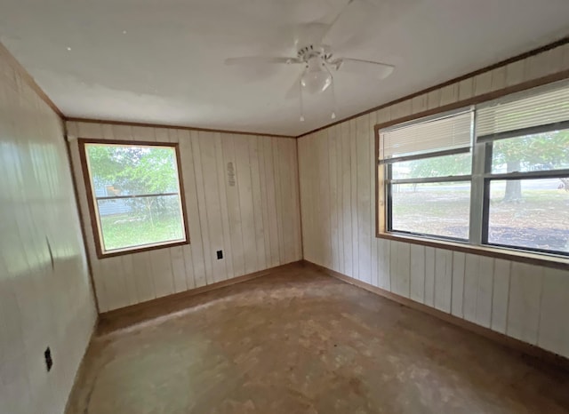 spare room with healthy amount of natural light, baseboards, a ceiling fan, crown molding, and wood walls