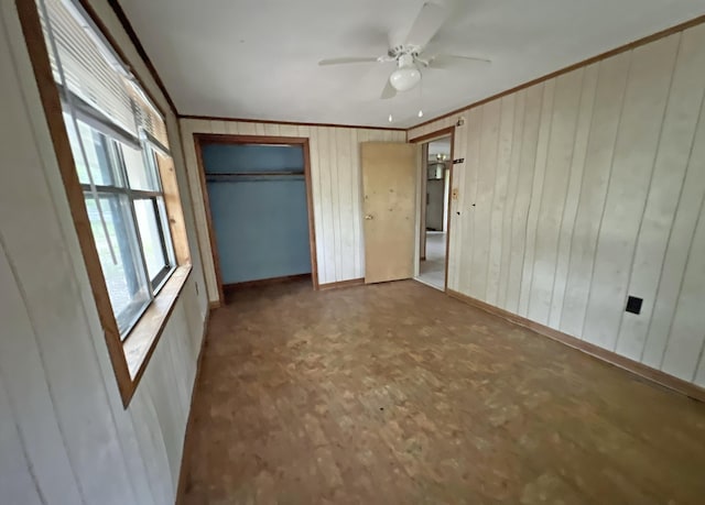 unfurnished bedroom with ornamental molding, baseboards, wooden walls, and a ceiling fan
