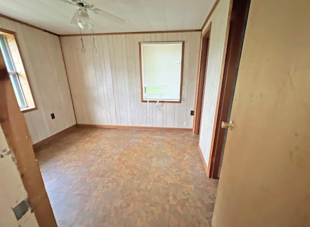 empty room with wood walls, baseboards, ceiling fan, and ornamental molding