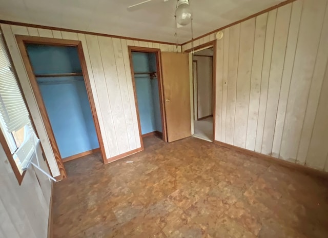 unfurnished bedroom featuring multiple closets, wooden walls, tile patterned floors, baseboards, and ceiling fan