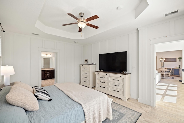 495 Brighton Cv, Freeport, FL 32439 - bedroom featuring a raised ceiling, a decorative wall, ensuite bathroom, a ceiling fan, and light wood-type flooring