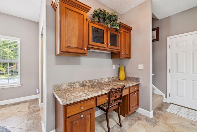 2009 Kildare Cir, Niceville, FL 32578 - kitchen with brown cabinetry, light stone countertops, baseboards, and glass insert cabinets