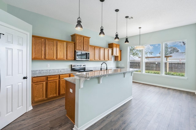 3167 Border Creek Dr, Crestview, FL 32539 - kitchen featuring appliances with stainless steel finishes, brown cabinets, dark wood-type flooring, light stone countertops, and a breakfast bar area