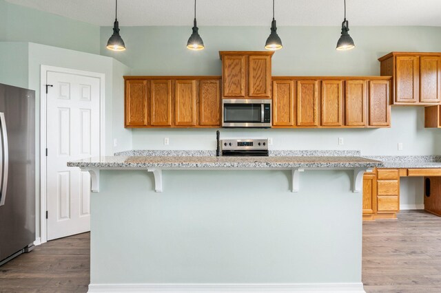 3167 Border Creek Dr, Crestview, FL 32539 - kitchen featuring appliances with stainless steel finishes, light wood finished floors, brown cabinets, pendant lighting, and light stone counters