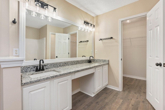 3167 Border Creek Dr, Crestview, FL 32539 - full bathroom with double vanity, wood finished floors, a spacious closet, baseboards, and a textured ceiling