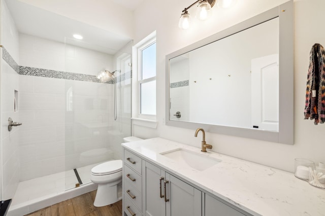 bathroom with toilet, a tile shower, vanity, and wood finished floors