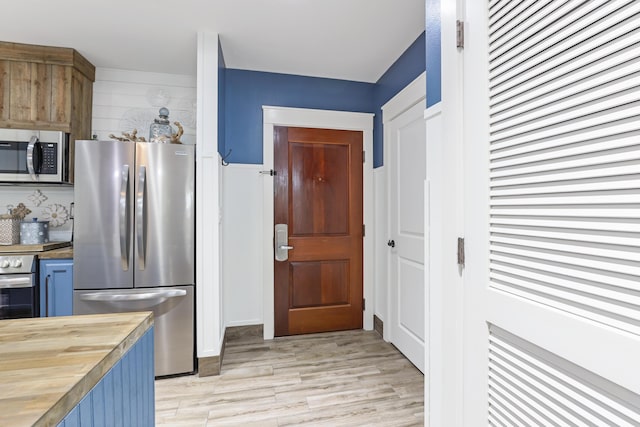 kitchen featuring stainless steel appliances, butcher block countertops, light wood-style flooring, and blue cabinetry