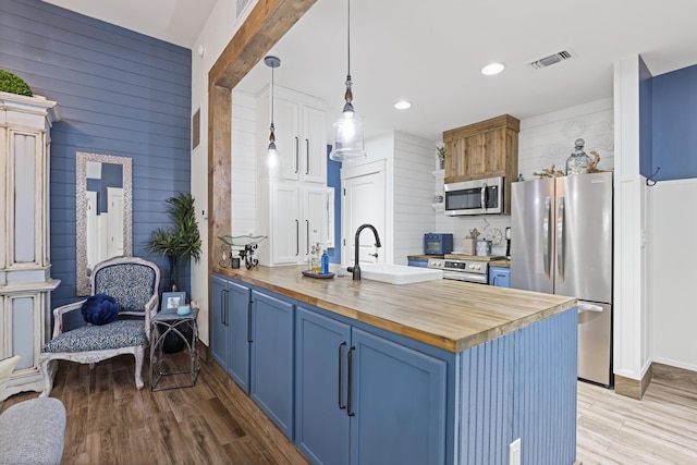kitchen featuring butcher block counters, appliances with stainless steel finishes, a sink, blue cabinets, and wood walls