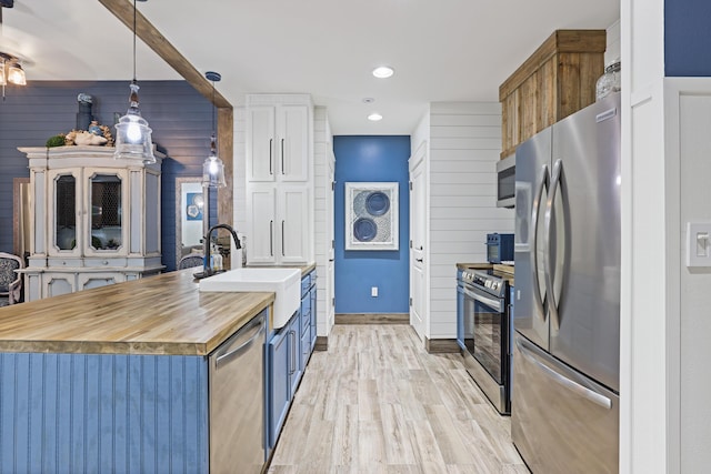 kitchen featuring appliances with stainless steel finishes, a sink, light wood-type flooring, wood counters, and hanging light fixtures