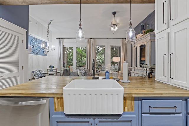 kitchen with butcher block countertops, stainless steel dishwasher, a sink, blue cabinetry, and hanging light fixtures