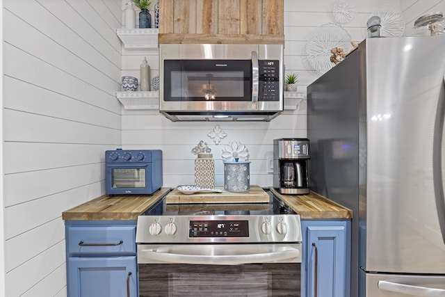 kitchen with appliances with stainless steel finishes, butcher block counters, and blue cabinets