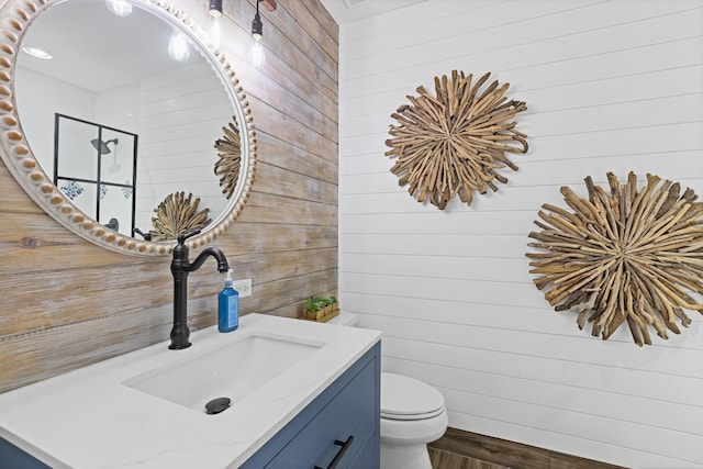 bathroom with wooden walls, toilet, vanity, and wood finished floors