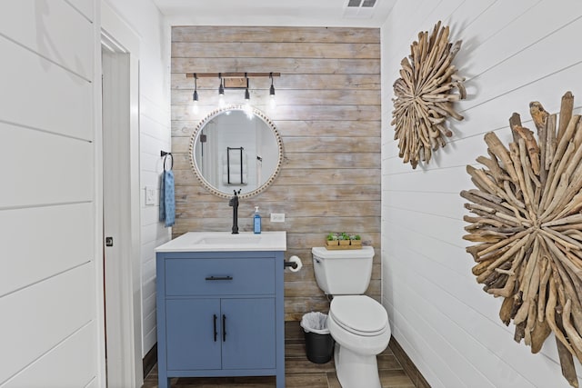bathroom featuring toilet, vanity, wood finished floors, and wooden walls