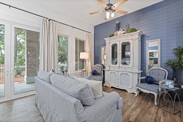 living room with light wood finished floors, a ceiling fan, and wooden walls