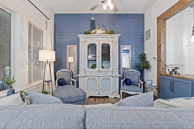 living area featuring wood finished floors, a ceiling fan, and wooden walls