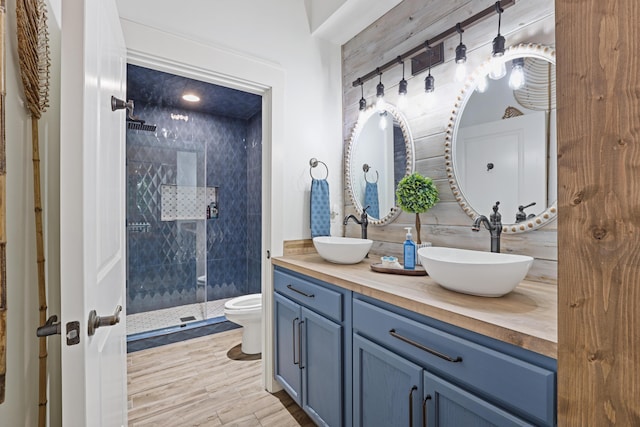full bath with a tile shower, toilet, double vanity, and wood finished floors