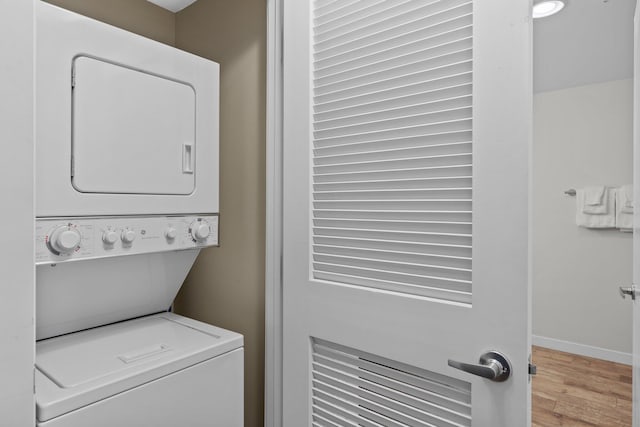 laundry room featuring stacked washer and clothes dryer, wood finished floors, and baseboards