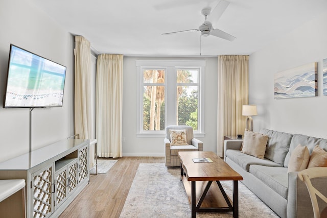 living area with light wood-style floors, a ceiling fan, and baseboards