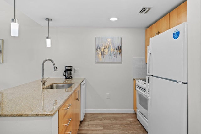kitchen with a sink, white appliances, light wood-style floors, a peninsula, and light stone countertops