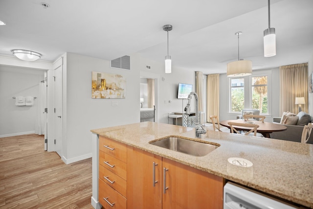 kitchen with a sink, light wood-style flooring, baseboards, open floor plan, and decorative light fixtures