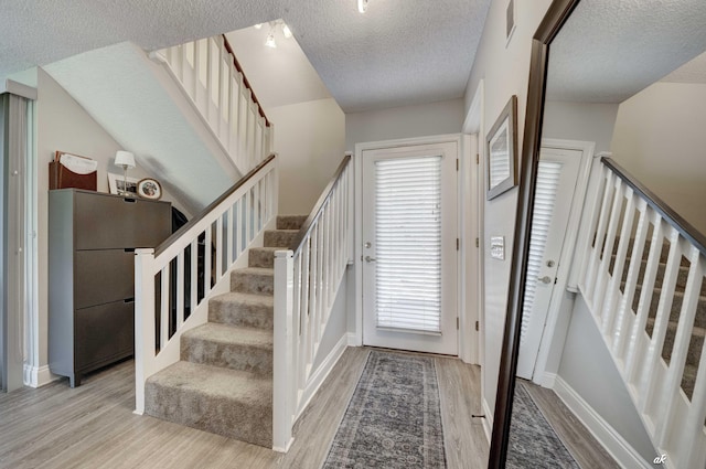 entrance foyer with stairs, wood finished floors, a textured ceiling, and baseboards