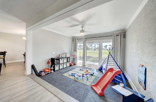 game room with a ceiling fan, crown molding, wood finished floors, a textured wall, and a textured ceiling
