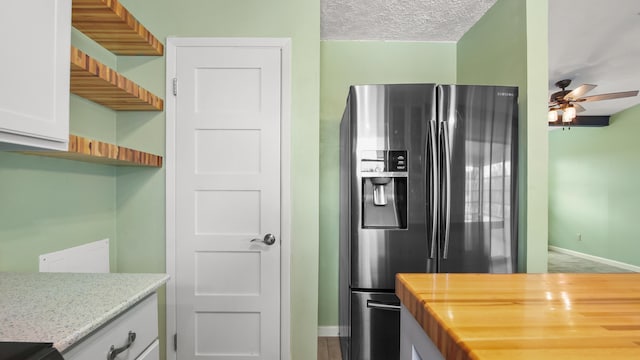 kitchen with fridge with ice dispenser, ceiling fan, baseboards, butcher block countertops, and white cabinets