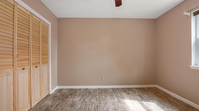 unfurnished bedroom with wood finished floors, a closet, baseboards, and a ceiling fan