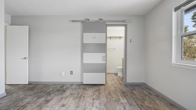 unfurnished bedroom with wood finished floors, baseboards, and ensuite bathroom