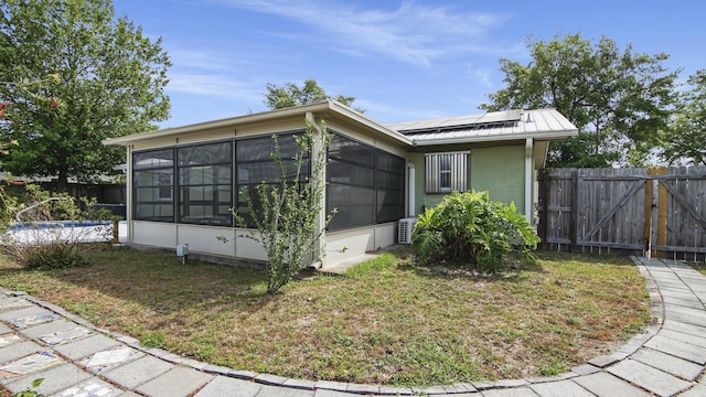view of property exterior featuring a sunroom, solar panels, a gate, fence, and stucco siding