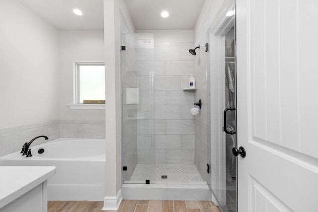 bathroom with a stall shower, a garden tub, wood finished floors, vanity, and recessed lighting