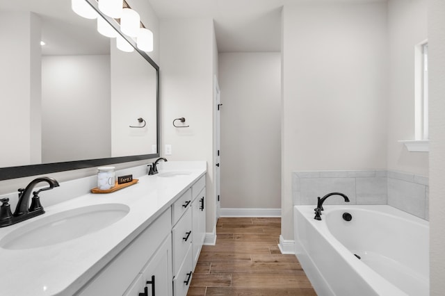 bathroom with wood finished floors, a bath, double vanity, and baseboards